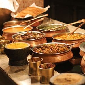 Un buffet di varie pietanze indiane, inclusi curry e riso, servite in tradizionali ciotole di rame su un piano di lavoro in pietra.