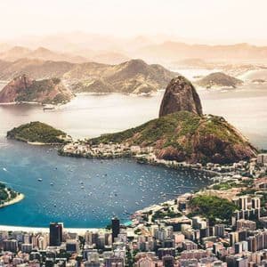 Una vista aerea di una vasta città costiera con una baia piena di barche incastonata tra montagne verdi e rocciose.