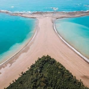 Una vista aerea di una formazione di spiaggia a forma di coda di balena con acqua turchese su entrambi i lati e una foresta verde alla base.