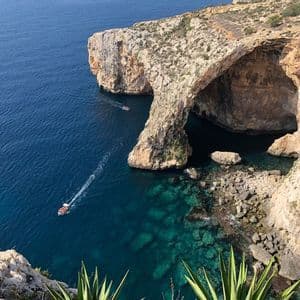 Eine Luftaufnahme eines großen natürlichen Felsbogens über dem Meer, mit zwei Booten, die durch das klare türkisfarbene Wasser fahren.