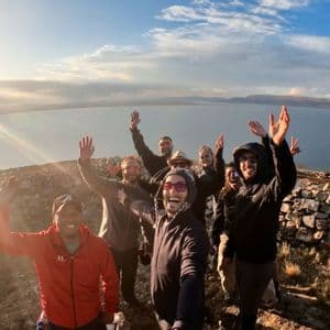 Eine WeRoad-Gruppe macht bei Sonnenuntergang ein Gruppenselfie auf einem Hügel mit Blick auf ein großes Gewässer.
