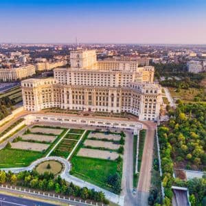 Una vista aérea de un gran y ornamentado edificio gubernamental rodeado de céspedes bien cuidados, carreteras y un vasto paisaje urbano al atardecer.