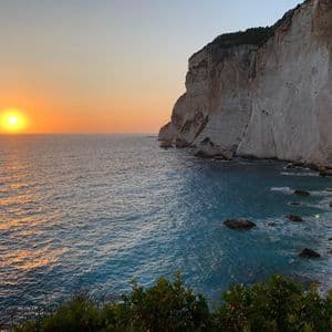 Die Sonne geht über einem ruhigen Meer unter, neben majestätischen weißen Kalksteinfelsen und unter klarem Himmel.