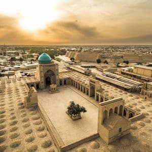 Ein Luftbild einer historischen Stadt bei Sonnenuntergang, mit einer großen Moschee mit einer türkisfarbenen Kuppel und einem zentralen Innenhof.