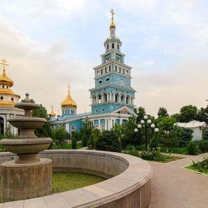 Plusieurs églises orthodoxes bleues aux dômes en oignon dorés se dressent dans un jardin avec une fontaine en pierre au premier plan.
