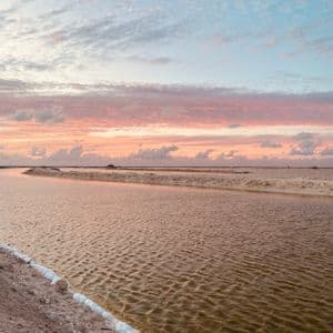 Salt pans with channels of water reflecting a colorful sunset sky with pink and blue clouds.