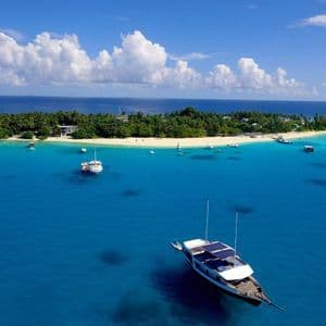 Aerial view of a tropical island with a white sand beach, surrounded by turquoise water and several anchored boats.