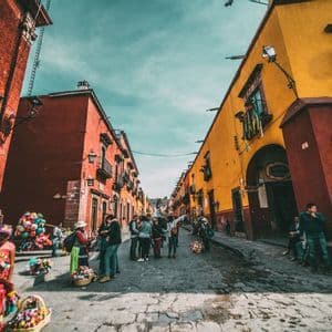 Un viaje en grupo de WeRoad en una concurrida calle empedrada entre edificios coloridos rojos y amarillos bajo un cielo brillante.