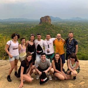 Eine WeRoad-Gruppe posiert für ein Foto an einem felsigen Aussichtspunkt mit Blick auf ein üppig grünes Tal und eine große Felsformation in der Ferne.