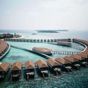 Vista aérea de un resort con bungalows sobre el agua dispuestos en curva sobre el océano turquesa.
