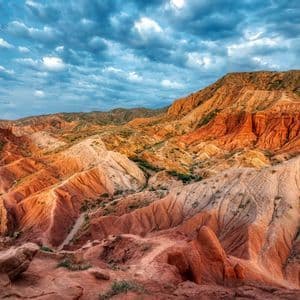 A wide view of an arid landscape of red and orange canyon formations under a cloudy blue sky.