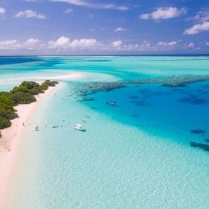 Una vista aerea di una lingua di sabbia tropicale con una spiaggia bianca, barriera corallina e barche in acqua cristallina turchese.