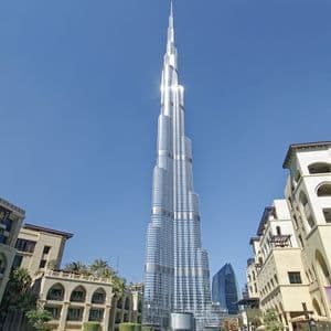 Un moderno grattacielo di vetro si erge su edifici in stile tradizionale sotto un cielo azzurro brillante.