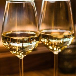 Un primo piano di due bicchieri di vino bianco, che riflettono le luci calde e soffuse della stanza.