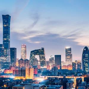 A panoramic view of a modern city skyline with numerous illuminated skyscrapers under a colorful dusk sky.