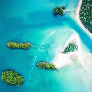 Une vue aérienne de bateaux à moteur naviguant entre de petites îles verdoyantes dans des eaux turquoise avec des bancs de sable blanc.