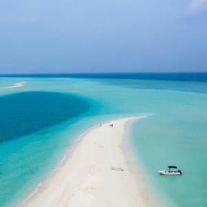 Una vista aerea di un viaggio di gruppo WeRoad su un banco di sabbia bianca che si snoda attraverso acque turchesi e blu profondo, con una barca vicina.