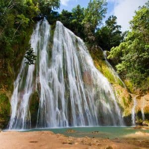 A wide waterfall cascades down a mossy rock face into a turquoise pool, surrounded by dense jungle foliage.