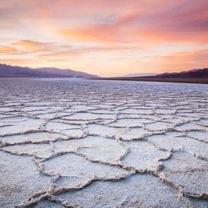 Distese di sale crepate si estendono verso montagne lontane sotto un cielo colorato al tramonto.