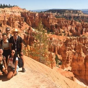 Un grupo de viaje de WeRoad posa para una foto en un mirador con vistas a un vasto cañón con agujas de roca naranjas.