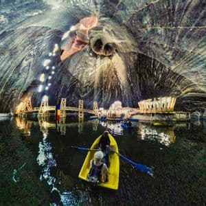 Eine Weitwinkelaufnahme von WeRoad-Gruppenteilnehmern, die in einer riesigen, beleuchteten unterirdischen Salzhöhle auf einem See Boote paddeln.