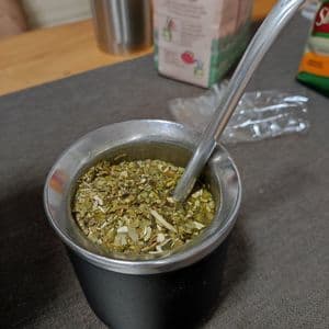 Un primo piano di una zucca da mate nera e argentata riempita con foglie di yerba mate e una cannuccia bombilla di metallo su un tavolo.
