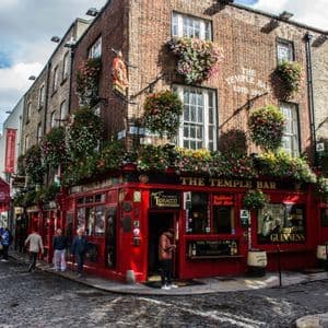 La façade rouge du pub The Temple Bar au coin d'une rue pavée, décorée de paniers de fleurs suspendus sous un ciel nuageux.