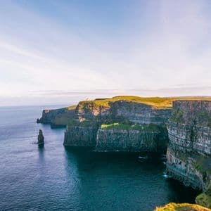 De hautes falaises rocheuses couvertes d'herbe verte surplombent une mer d'un bleu foncé avec un piton rocheux proéminent.