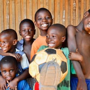 Seis niños sonriendo y riendo juntos, posando con un balón de fútbol frente a una pared de madera.