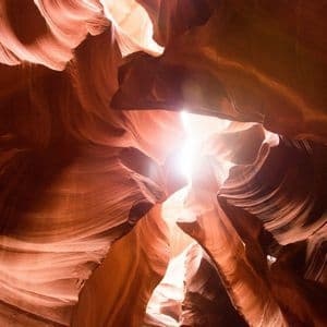 La luce del sole si riversa in uno stretto canyon, illuminando le texture delle pareti ondulate di arenaria rossa.