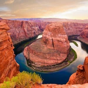 Una vista grandangolare di un fiume che serpeggia attorno a una massiccia formazione rocciosa rossa all'interno di un profondo canyon al tramonto.