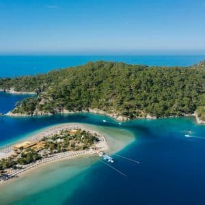 Una vista aerea di una lingua di sabbia con ombrelloni, che separa una laguna turchese dal mare blu profondo, accanto a una costa boscosa.