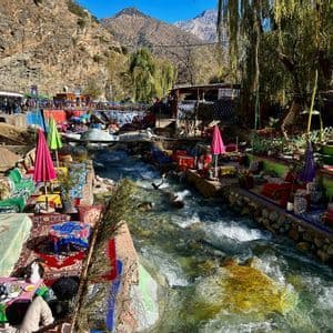 Asientos coloridos de cafetería al aire libre con alfombras y cojines están dispuestos a lo largo de las orillas de un río caudaloso en un valle de montaña.