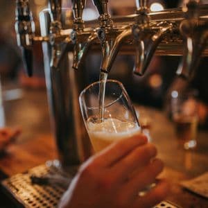 A close-up of a hand holding a glass while beer is poured from a shiny tap at a bar.