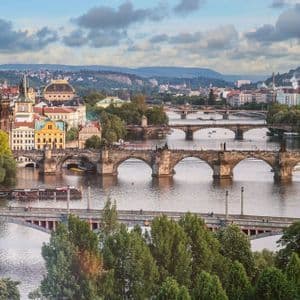 Una vista diurna di più ponti ad arco in pietra che attraversano un ampio fiume che scorre attraverso una città storica con colline sullo sfondo.
