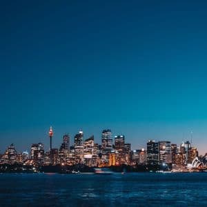 Uno skyline cittadino illuminato con grattacieli ed edifici moderni, visto da uno specchio d'acqua al crepuscolo.