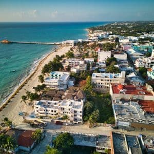 An aerial view of a coastal town with a sandy beach and a long pier extending into the turquoise ocean.