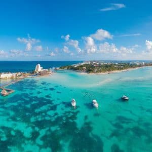 Vista aerea di una penisola tropicale con resort e barche ancorate in acqua cristallina e turchese sotto un cielo blu con nuvole.