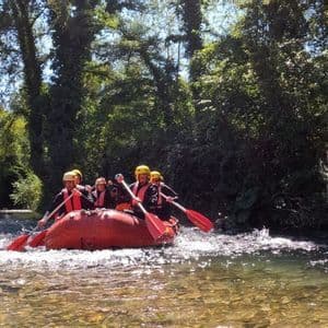 Un viaggio di gruppo WeRoad pagaia su un gommone rosso lungo un fiume, circondato da una fitta foresta verde sotto un cielo soleggiato.