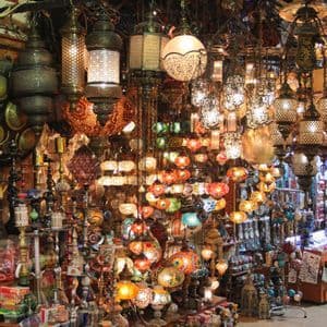 Una bancarella di mercato al coperto è fittamente stipata di lanterne a mosaico, illuminate e colorate, appese dall'alto e disposte sui banconi.