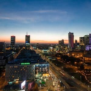 Luftaufnahme einer beleuchteten Stadtsilhouette bei Dämmerung, mit Wolkenkratzern und geschäftigen Straßen darunter.