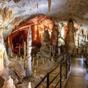 Un sendero pavimentado con pasamanos atraviesa una gran cueva iluminada con muchas estalactitas y estalagmitas.