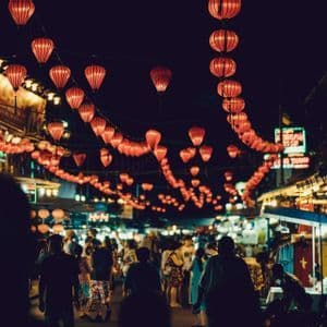 Lanterne rosse luminose pendono sopra un affollato mercato notturno.