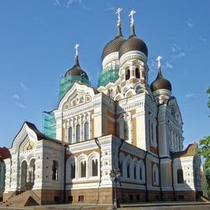 Una sontuosa cattedrale ortodossa con cupole a cipolla scure e croci dorate, parzialmente coperta da impalcature, sotto un cielo azzurro.
