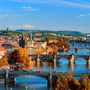 Une vue panoramique d'une ville européenne en automne, avec plusieurs ponts enjambant une rivière sous un ciel bleu clair.