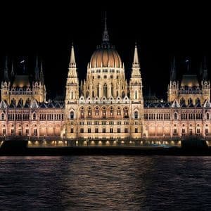 Un grand bâtiment orné d'un dôme central est brillamment éclairé la nuit à travers un plan d'eau.