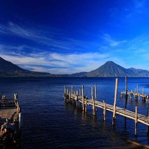 Pontili in legno si estendono in un lago blu calmo con grandi montagne sullo sfondo sotto un cielo parzialmente nuvoloso.