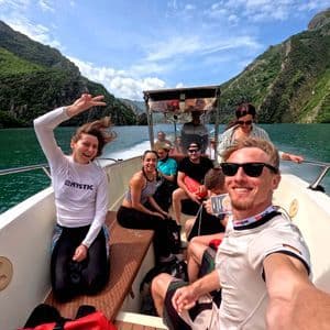 A WeRoad group trip takes a selfie on a boat surrounded by steep, green mountains and blue water.