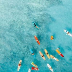 Veduta aerea di un viaggio di gruppo WeRoad su tavole da surf colorate che galleggiano in acqua limpida e turchese.