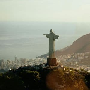 La statua del Cristo Redentore si erge su una montagna che domina una città costiera, con folle sulla piattaforma panoramica sottostante.